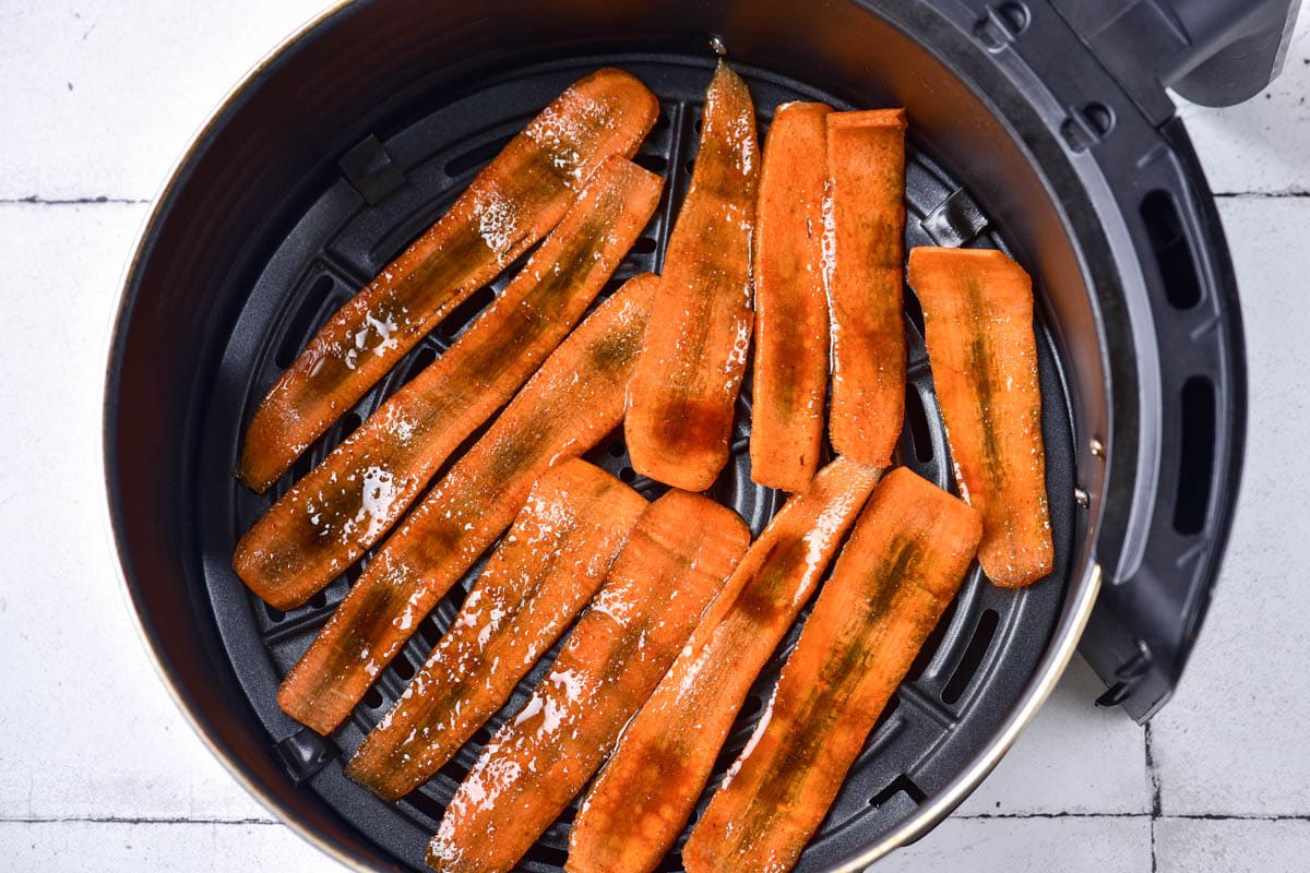 marinated raw slices of carrot in round black air fryer basket.