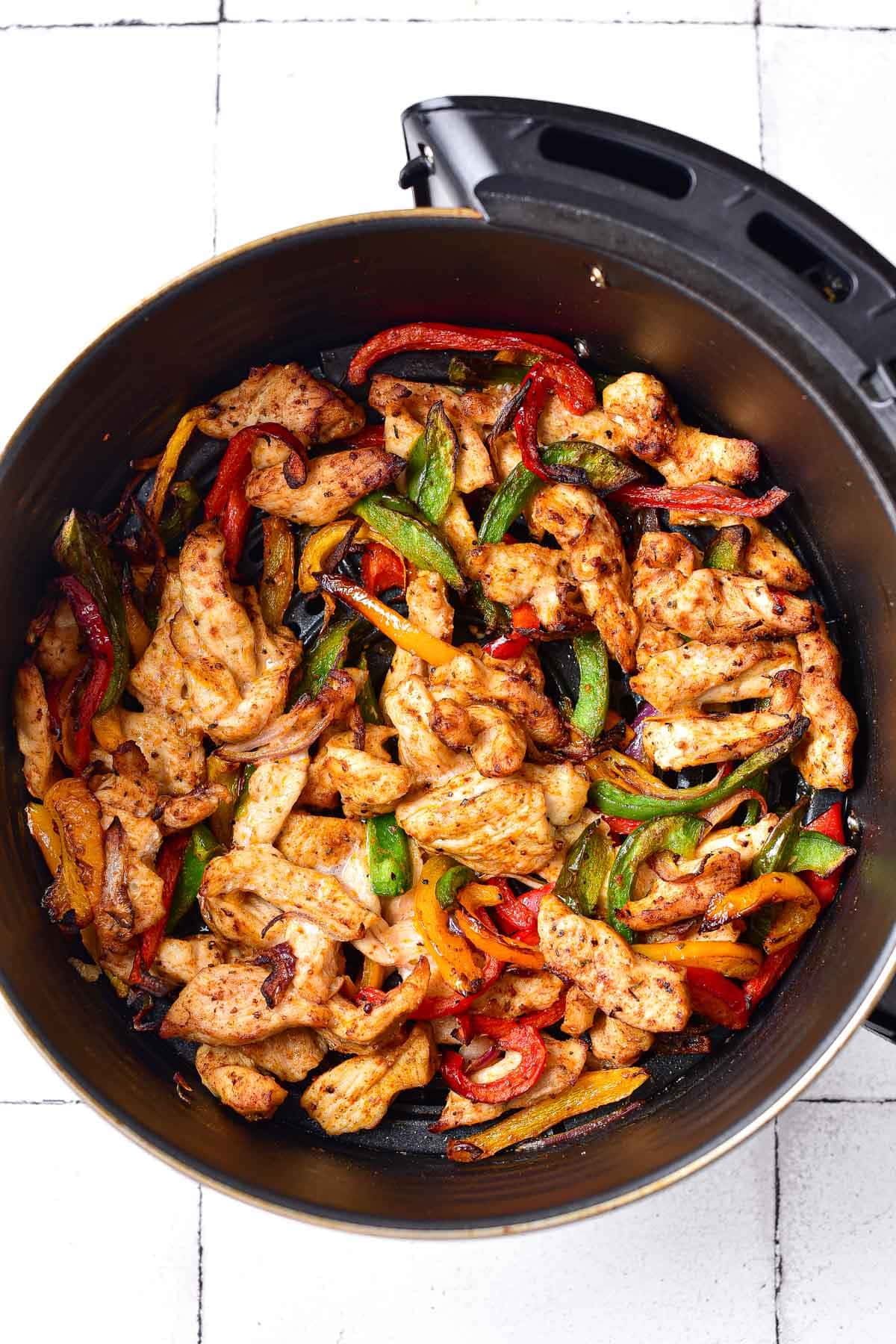 cooked chicken and peppers in round black air fryer basket.