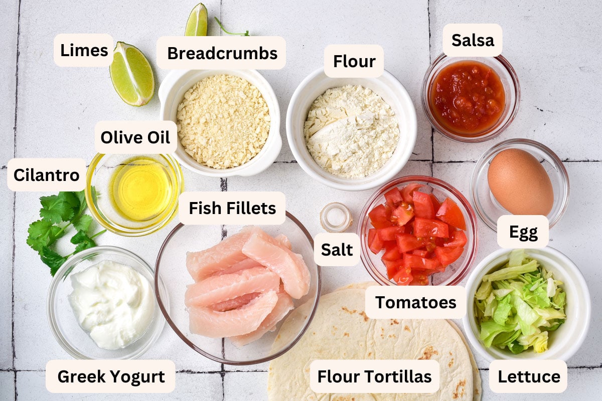 ingredients to make fish tacos in bowls with labels on a white counter.