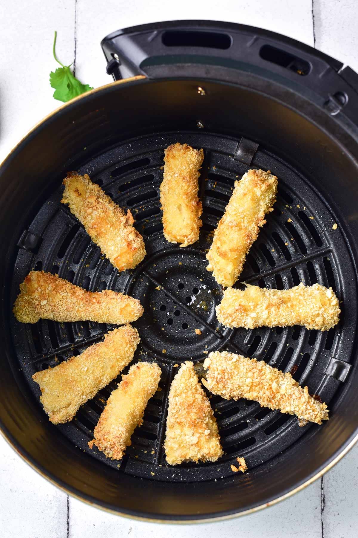 crispy pieces of breaded fish in round black air fryer basket.