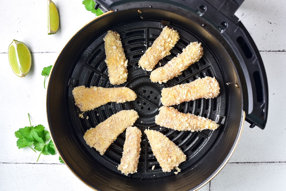 pieces of raw breaded fish arranged in a circle in a black air fryer basket.