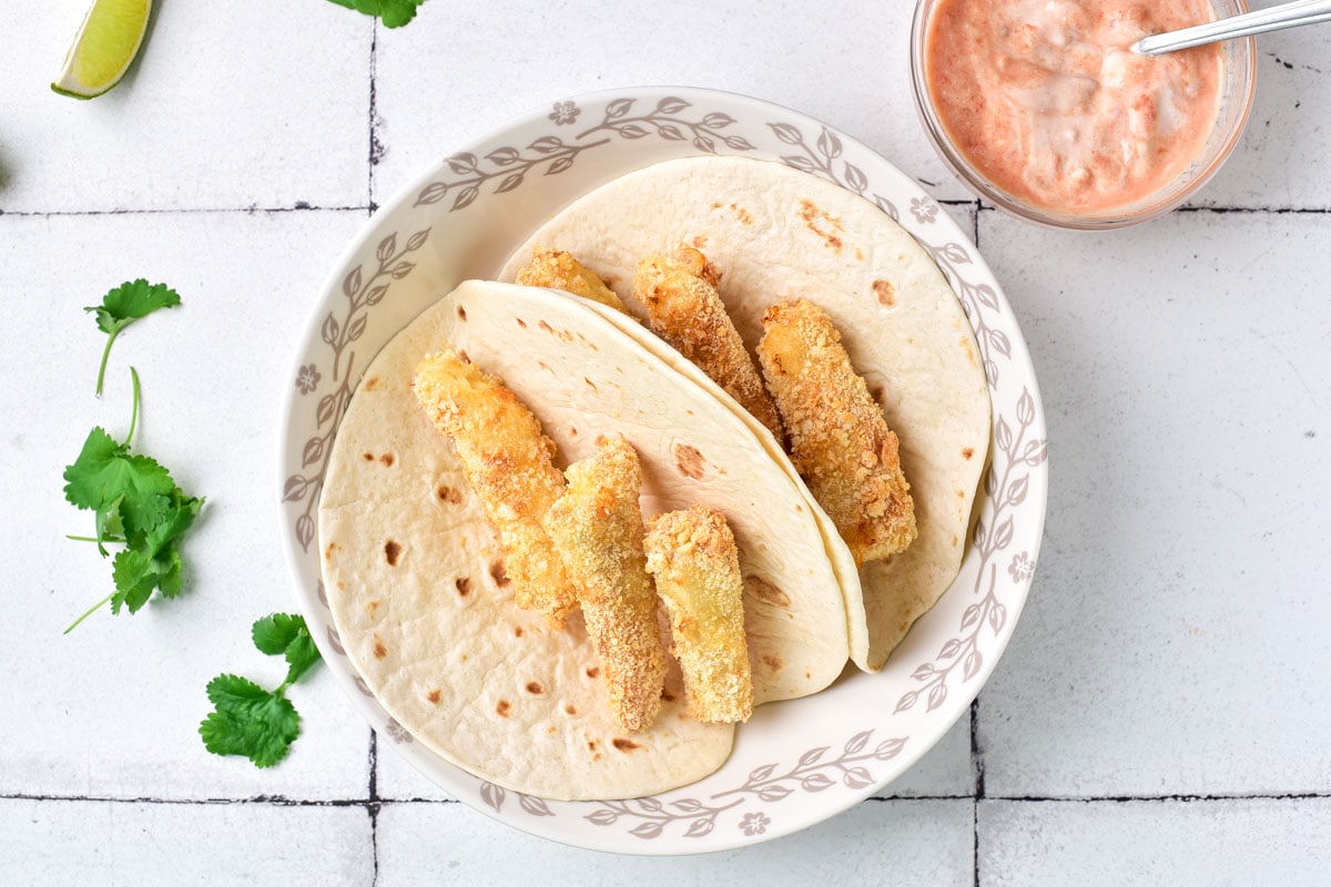 breaded fish pieces arranged in open flour tortillas on a plate.