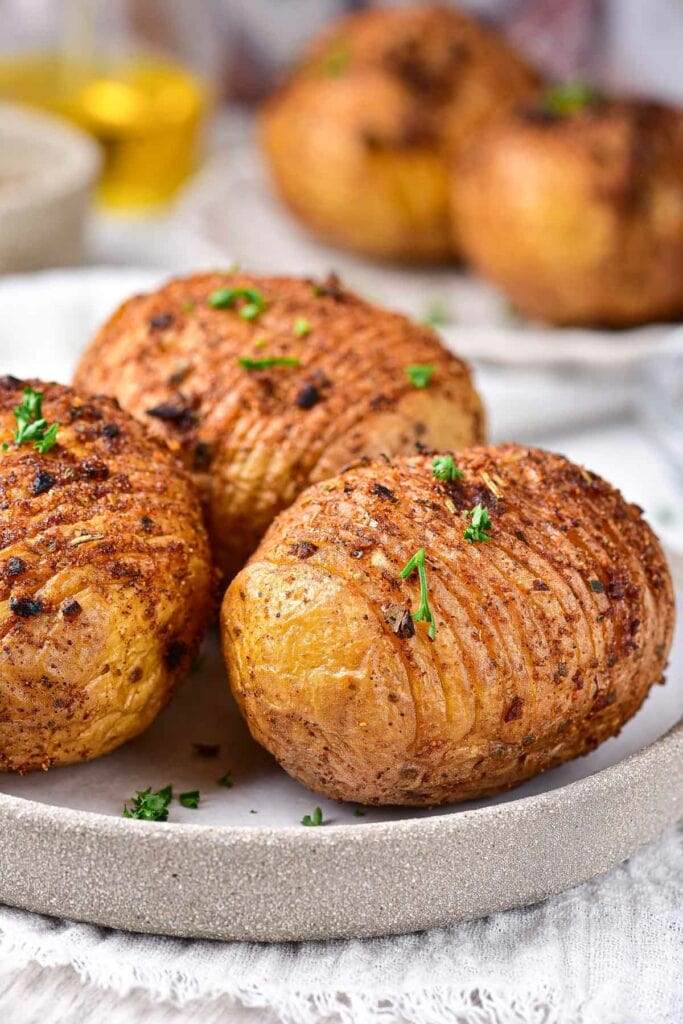 cooked hasselback potatoes with slits in them on plate with green parsley on top.