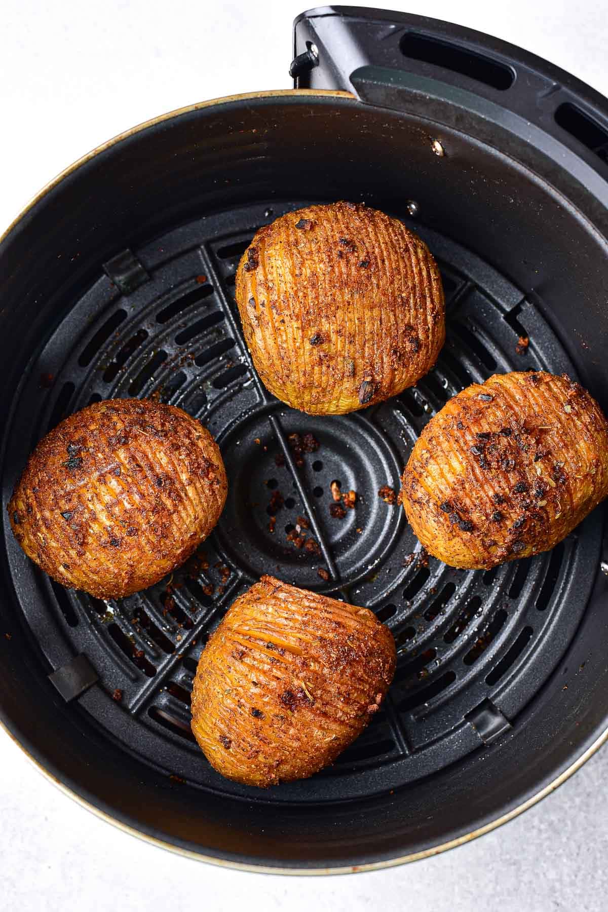four crispy hasselback potatoes sitting in round air fryer basket.