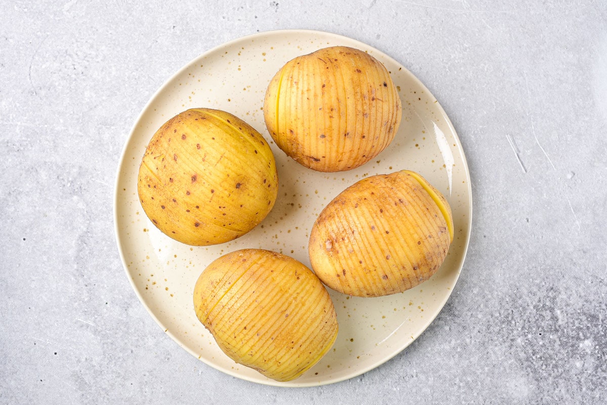 four potatoes on plate with slices in the tops of them.