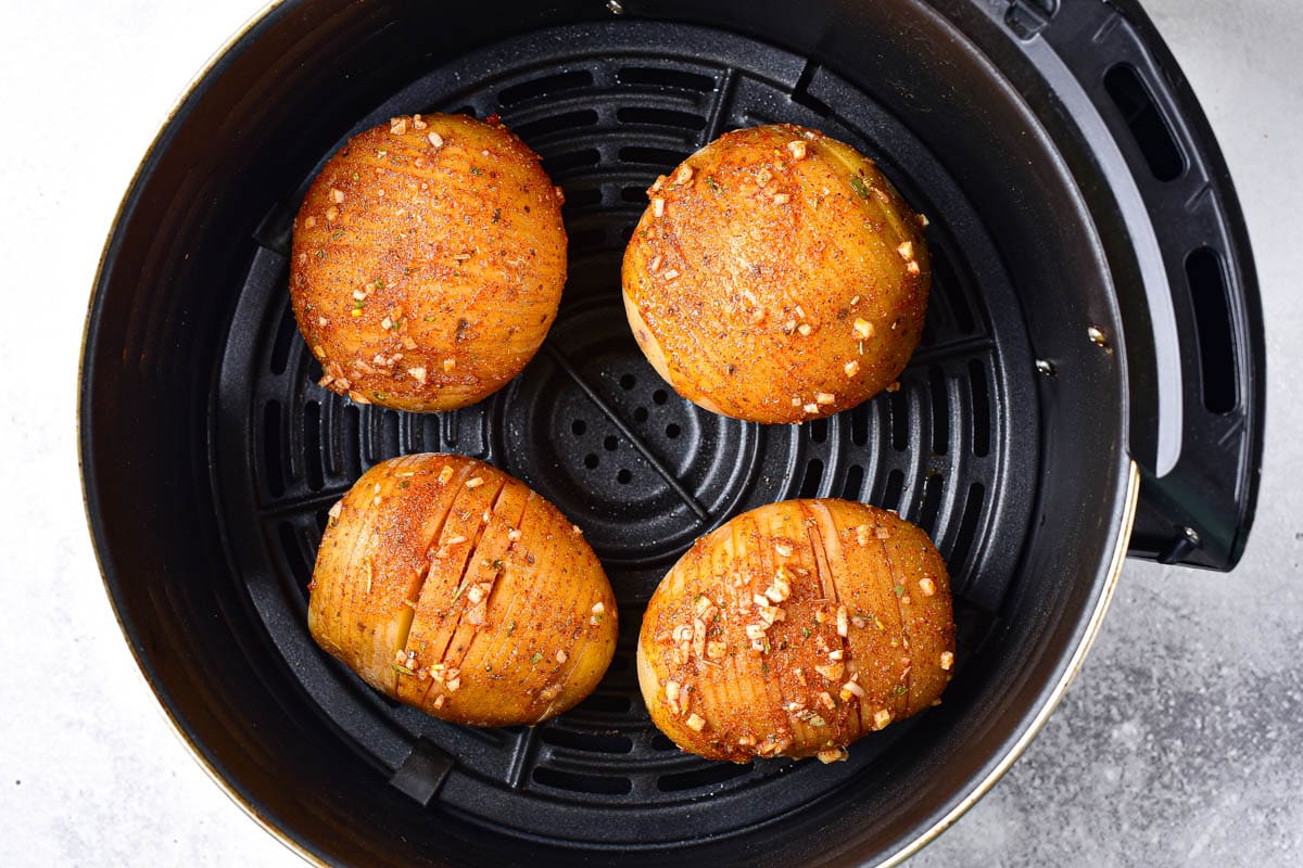 raw potatoes covered in oil and spices sitting in black round air fryer basket.