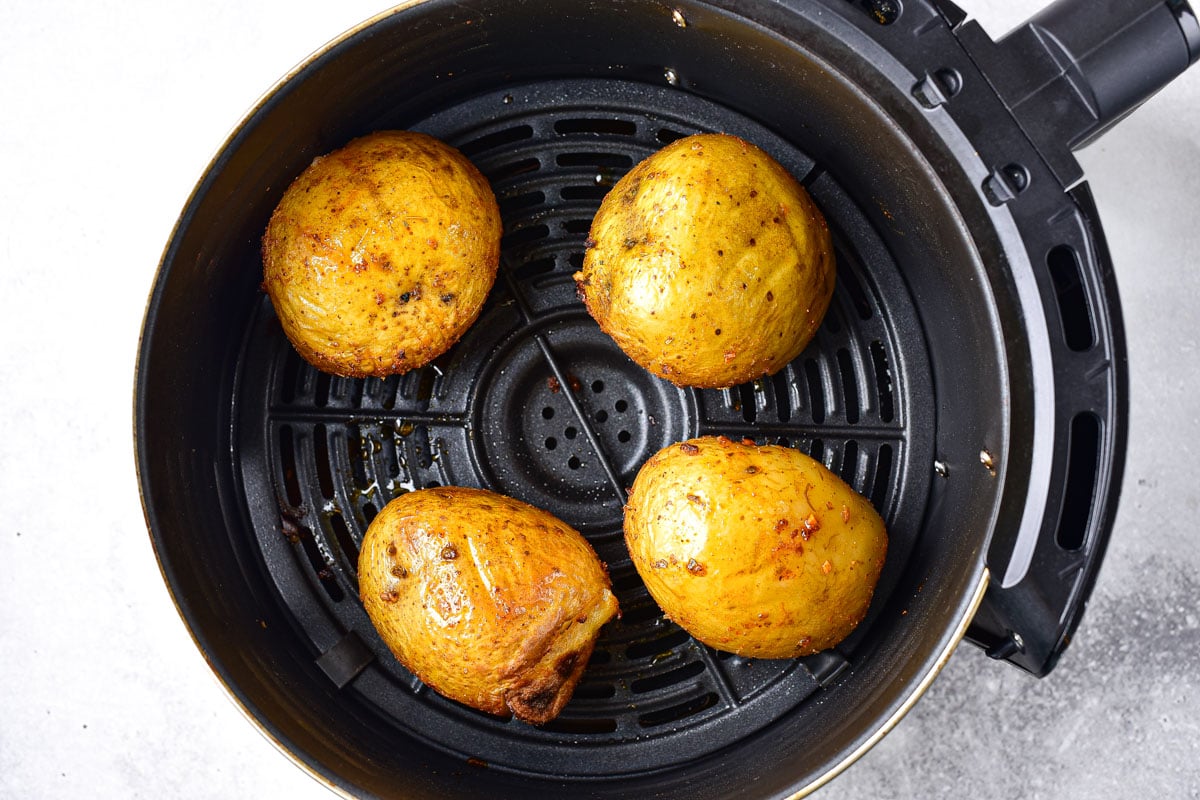 four round potatoes in black air fryer basket on counter.