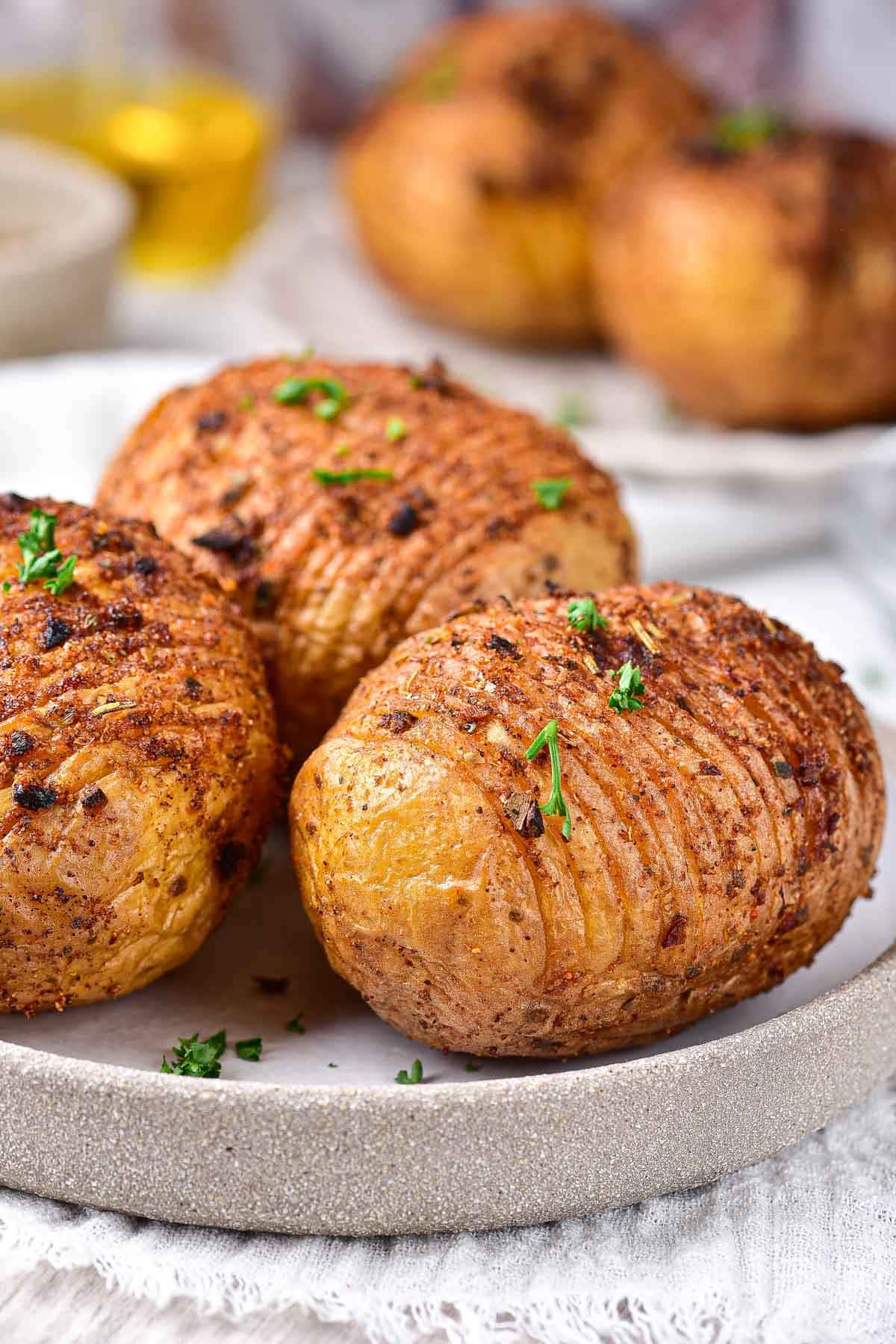 cooked hasselback potatoes with slits in them on plate with green parsley on top.
