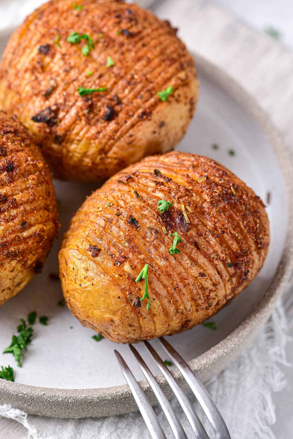 hasselback potatoes on round plate with chopped green parsley on top and fork beside.