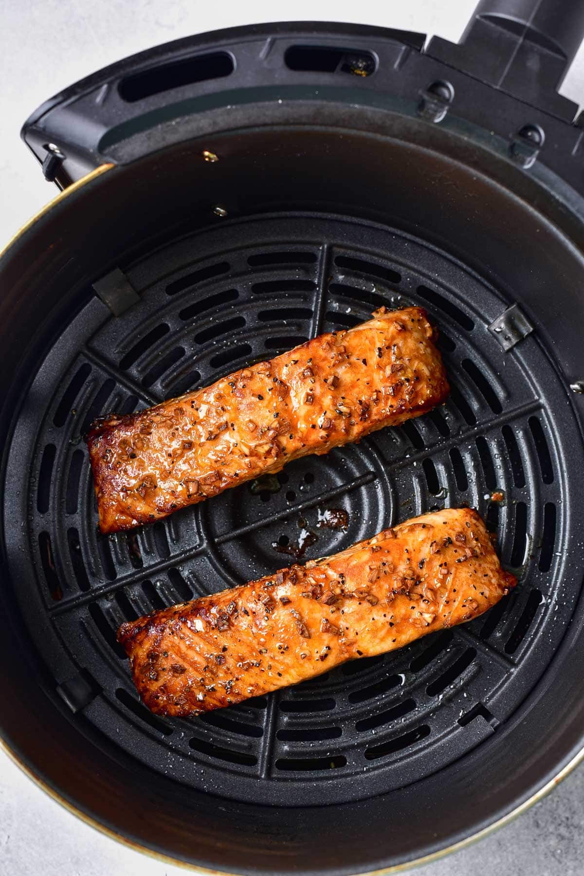 two cooked fillets of salmon in round black air fryer basket.