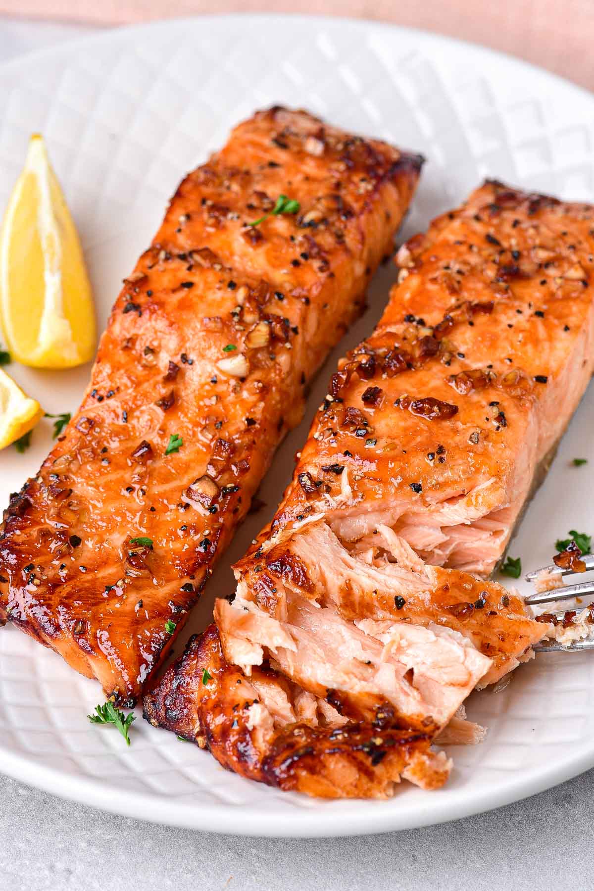 two filets of cooked honey garlic salmon one with flakes pulled away.