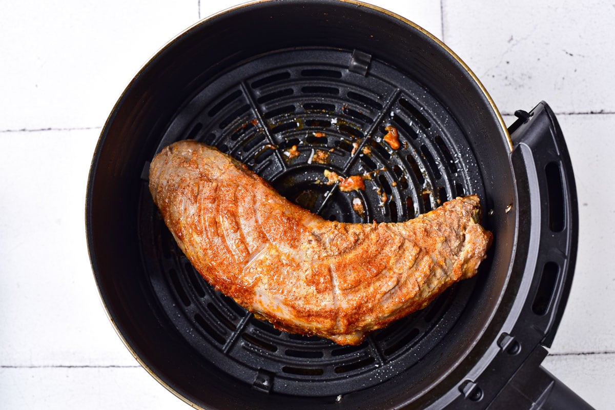 cooked pork tenderloin in round black air fryer basket on counter.