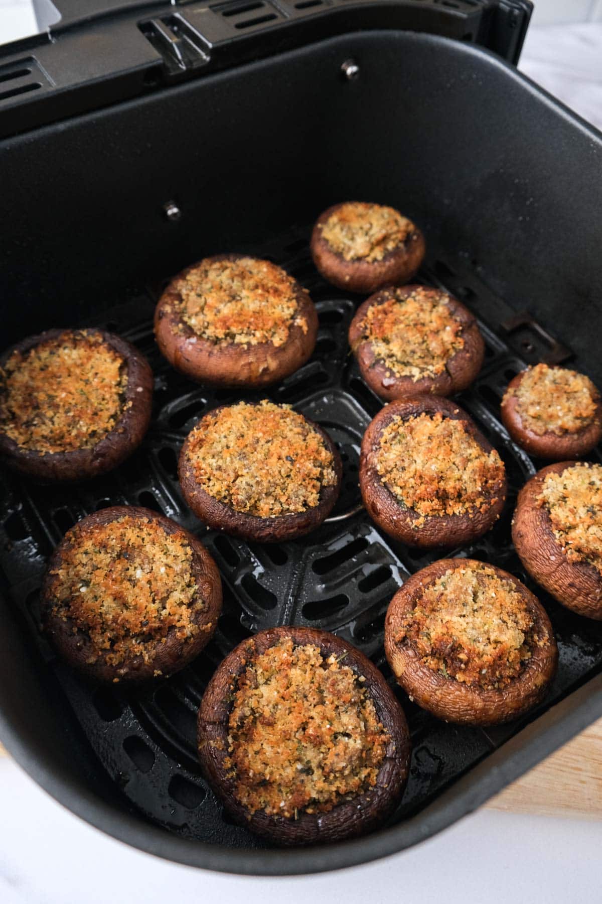 roasted stuffed mushroom caps in black air fryer tray with counter underneath.