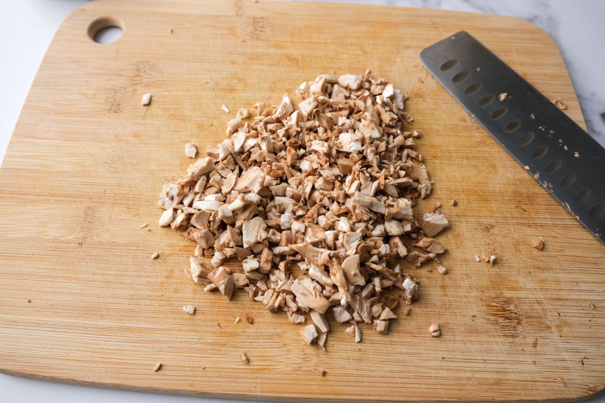 finely chopped mushrooms on wooden cutting board with knife beside.