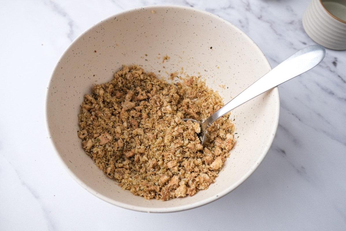 breadcrumbs mixed with oil and spices in white bowl with silver spoon sticking out.