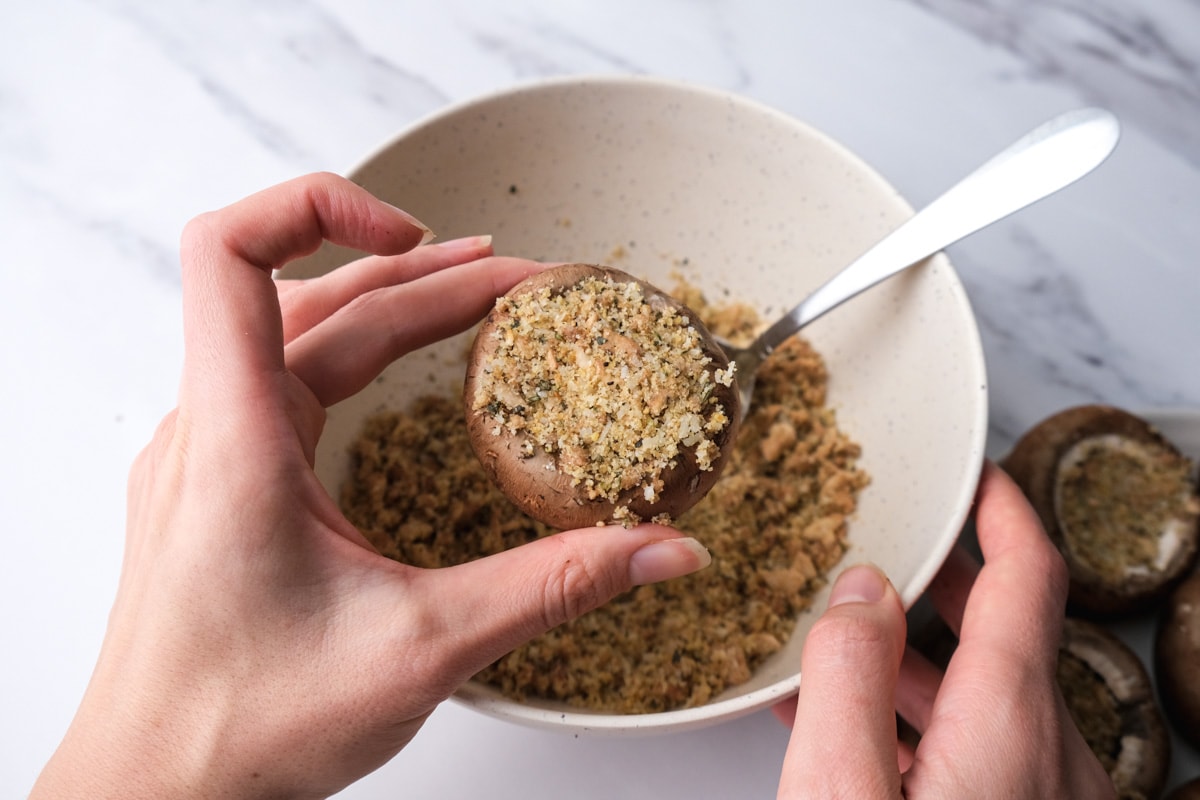 hand holding mushroom cap filled with breadcrumb mix.