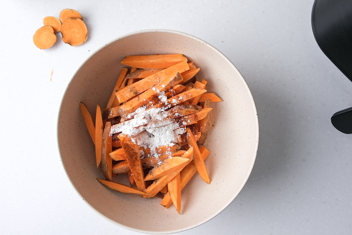 raw sweet potato fries on mixing bowl with spices on top not mixed in.