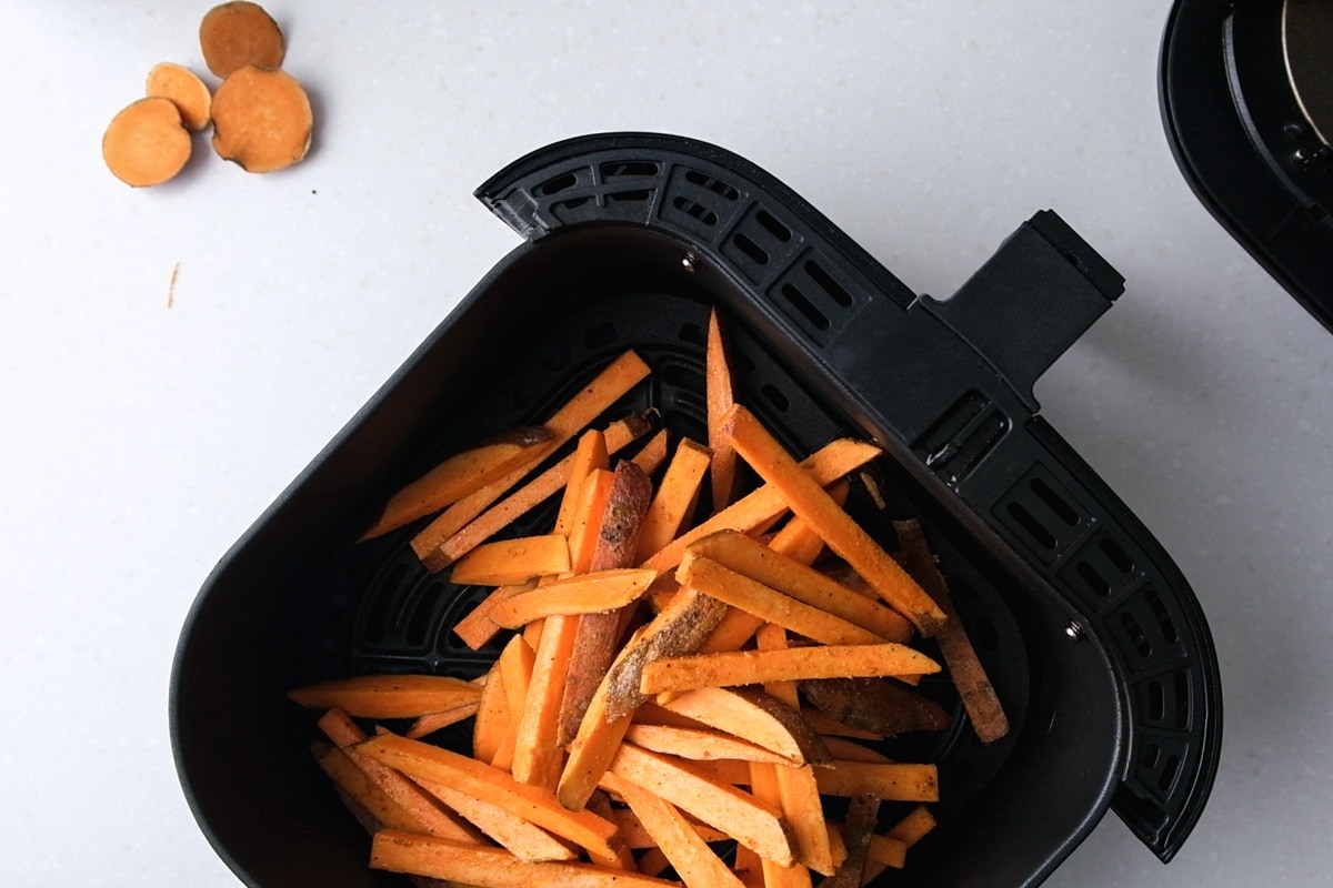 raw sweet potato fries in black air fryer tray on counter.