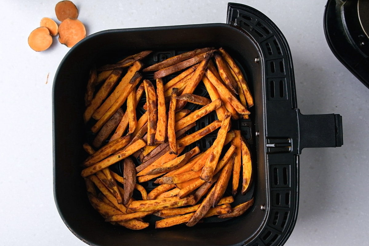 crispy cooked sweet potato fries in black air fryer basket on counter.