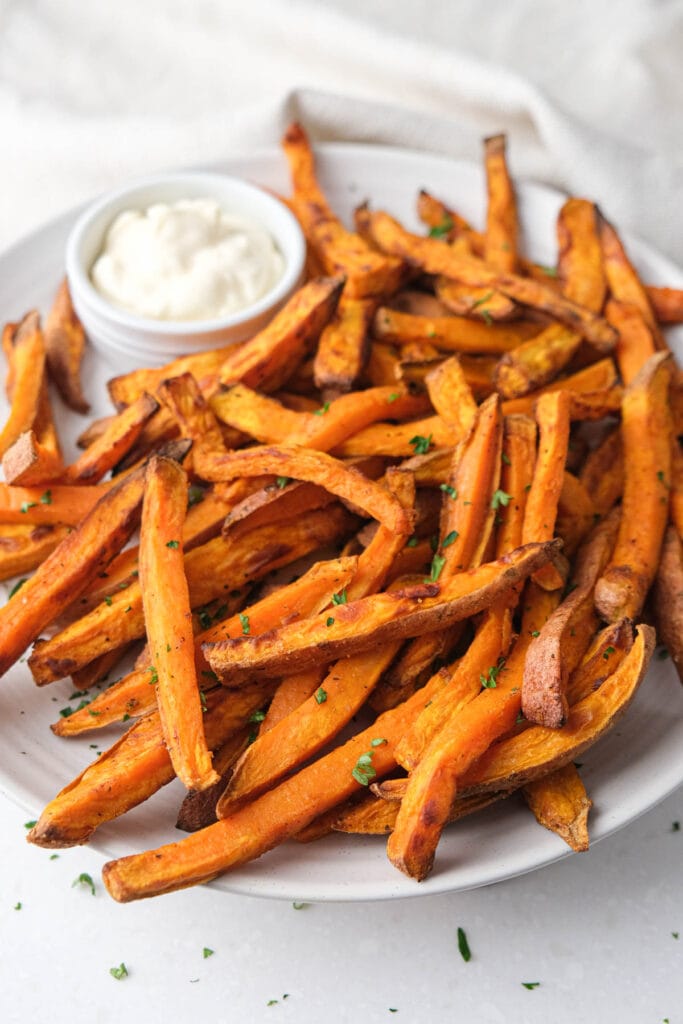 crispy sweet potato fries on plate with mayo dip behind.