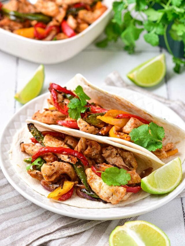 two chicken fajitas sitting on white plate with lime wedges around.