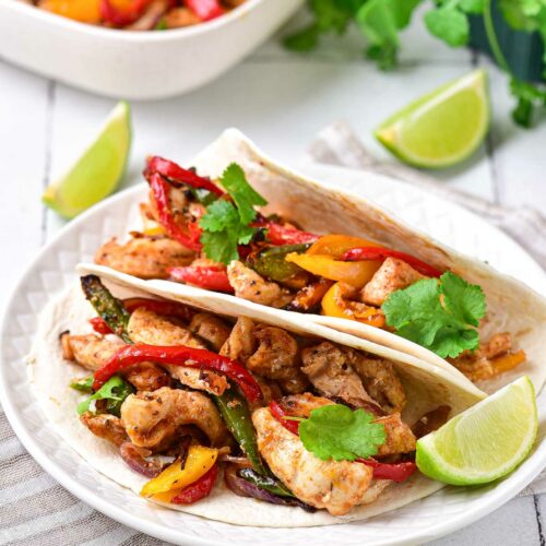 two chicken fajitas sitting on white plate with lime wedges around.