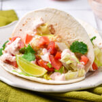 fish taco in tortilla on plate sitting on green cloth.