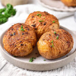 three cooked hasselback potatoes on plate on grey counter.