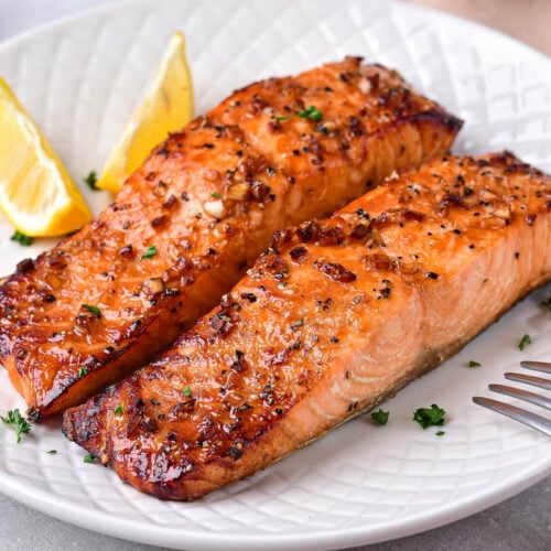 two cooked filets of honey garlic salmon on white plate.