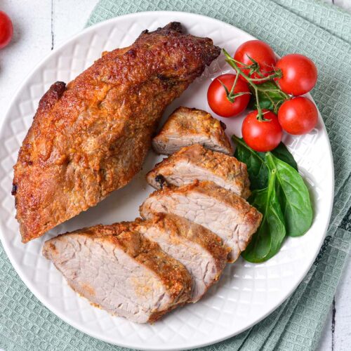 slices of pork tenderloin with red cherry tomatoes on white plate.