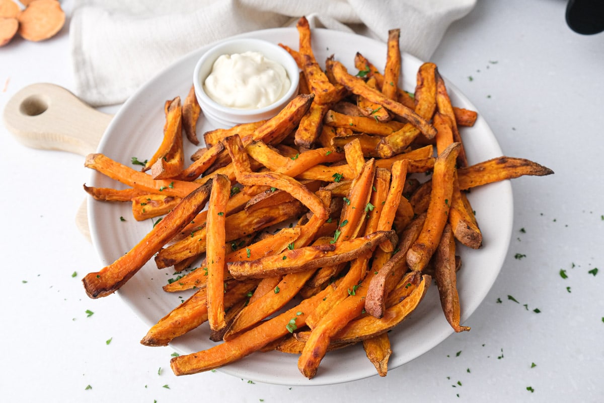sweet potato fries on white plate with dip behind and chopped parsley around.