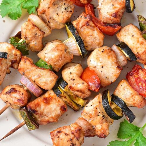 grilled pieces of chicken and vegetables on wooden skewers on plate.