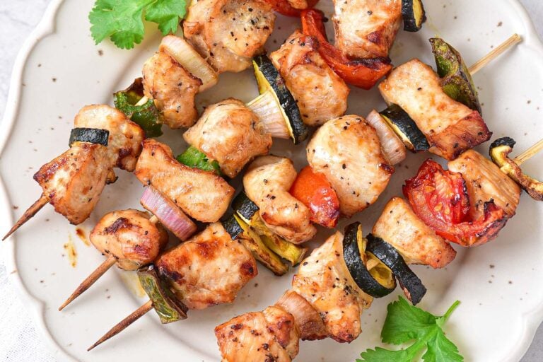 grilled pieces of chicken and vegetables on wooden skewers on plate.