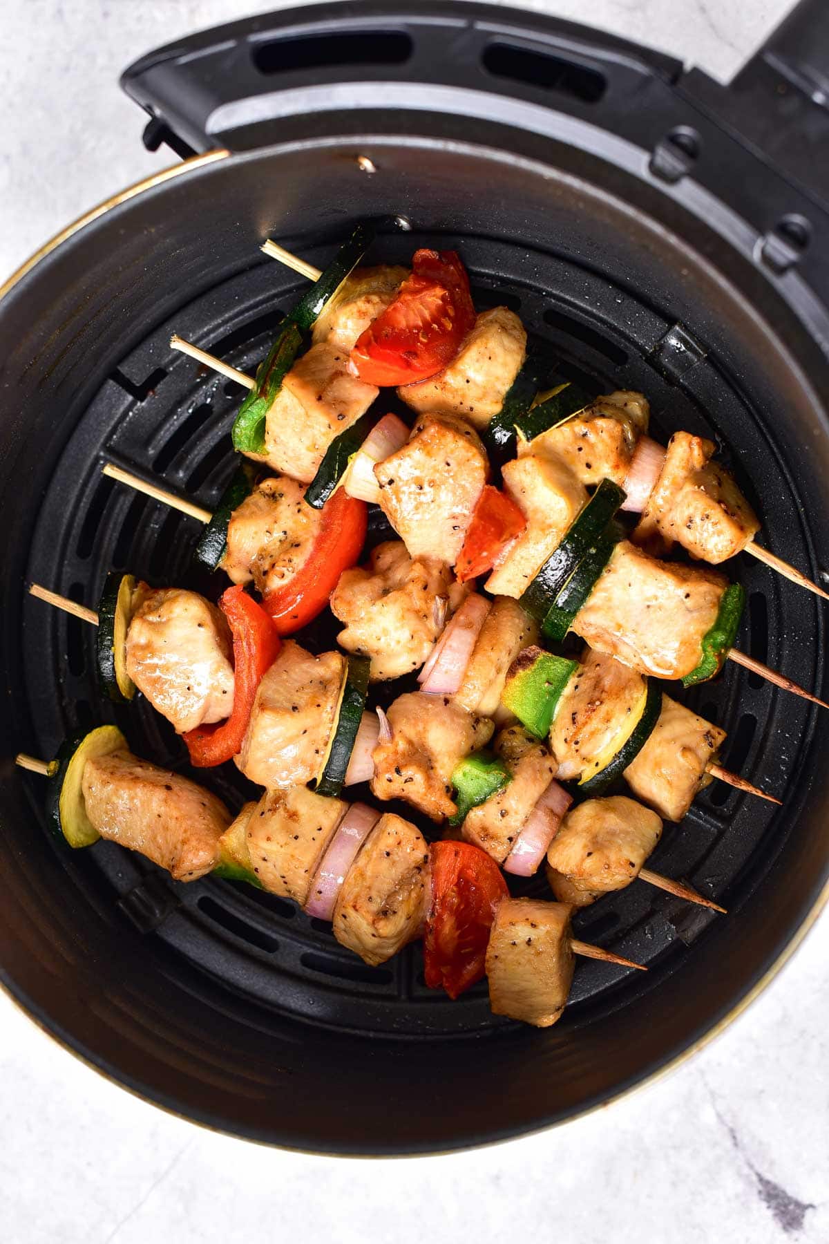 cooked chicken kabobs in black round air fryer basket seen from above.