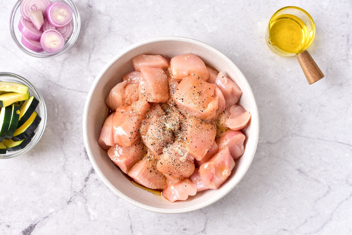 raw chunks of chicken breast in white bowl on counter with oil beside.