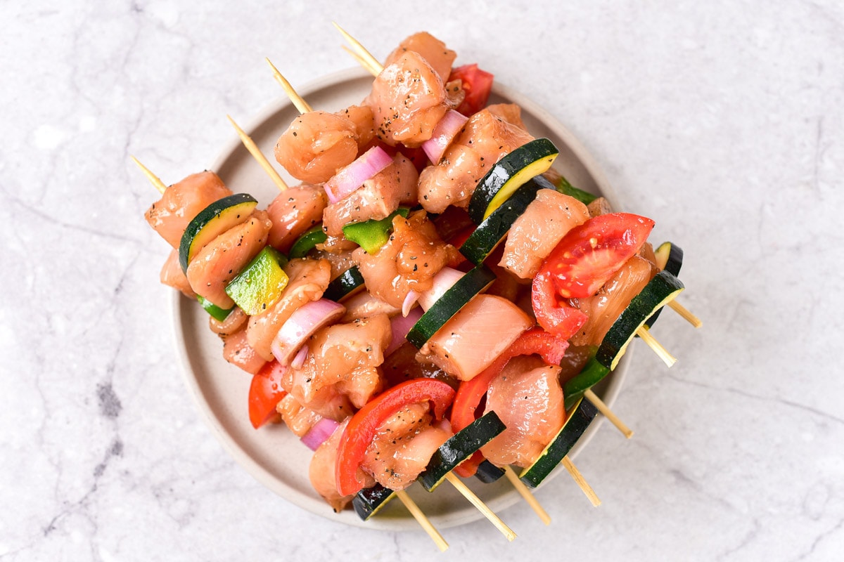 assembled raw chicken kabobs on wooden skewers sitting in a row on plate.