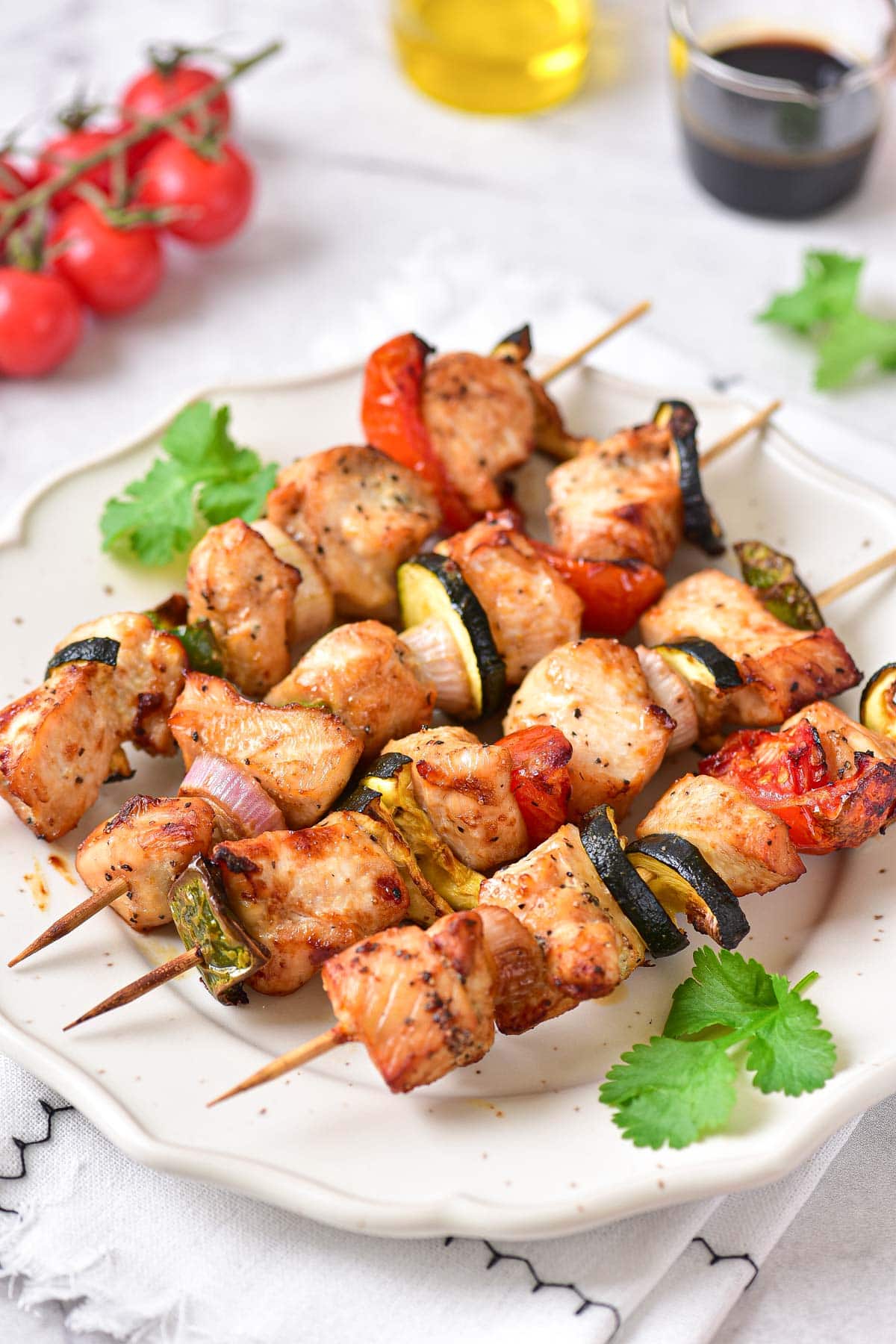 row of cooked chicken kabobs on white plate with green parsley around.