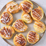 cinnamon rolls drizzled in white icing on large plate sitting on marble counter top.