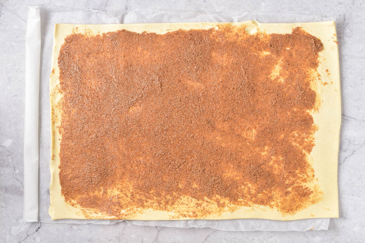 cinnamon butter and sugar blend spread out on flattened puff pastry on counter.