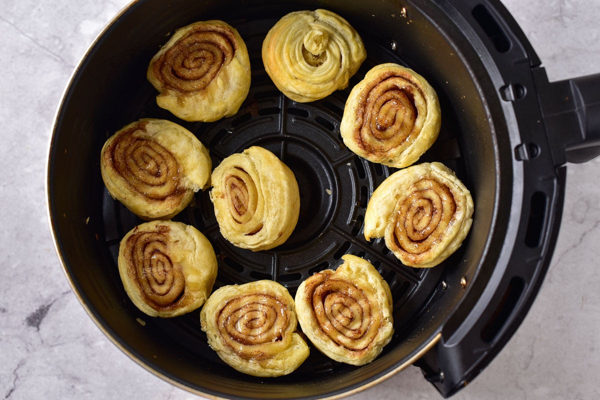 air fried cinnamon rolls in round black air fryer tray on marble counter.