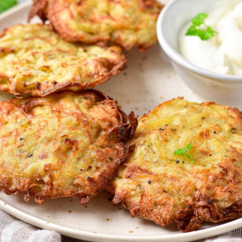 crispy potato pancakes on plate with sour cream and herbs beside.