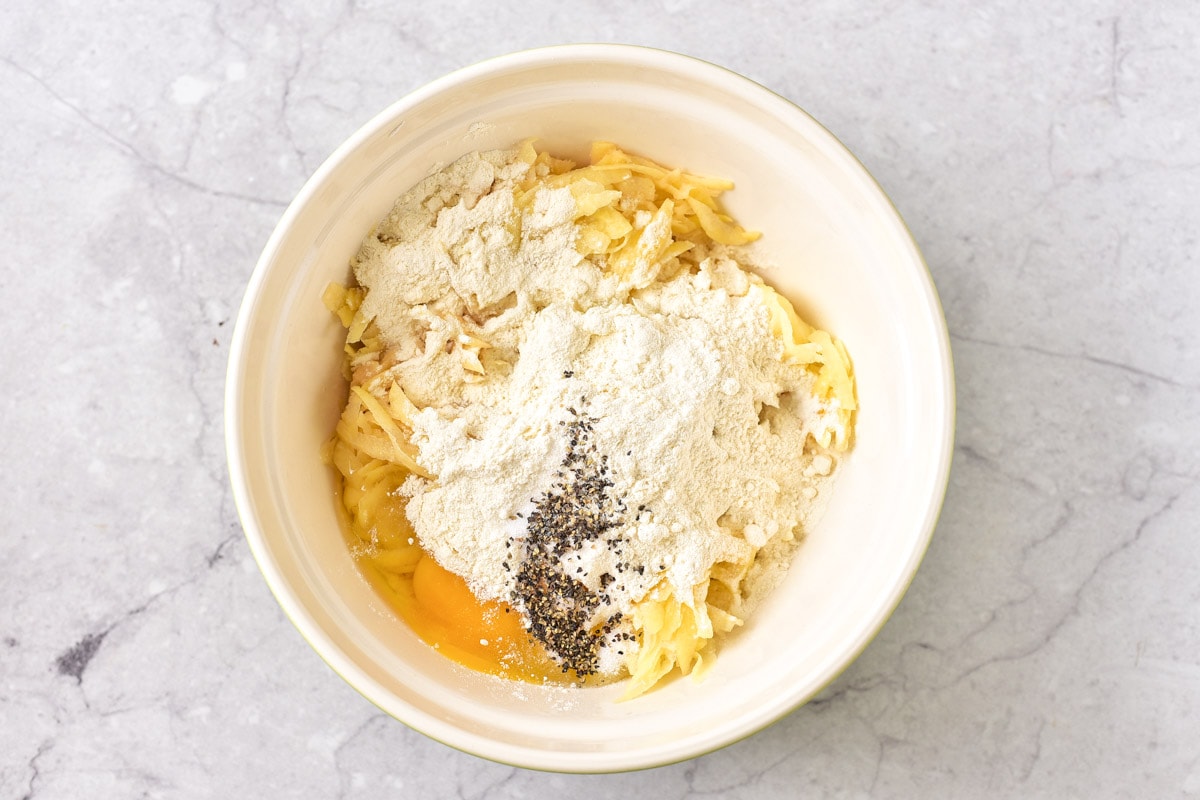 raw shredded potato and raw egg in white bowl with spices like pepper on top.