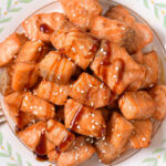 plate with crispy salmon bites covered in sauce and sesame seeds.
