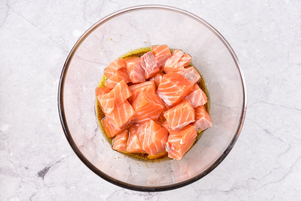 raw salmon cubes sitting in glass mixing bowl full of marinade.
