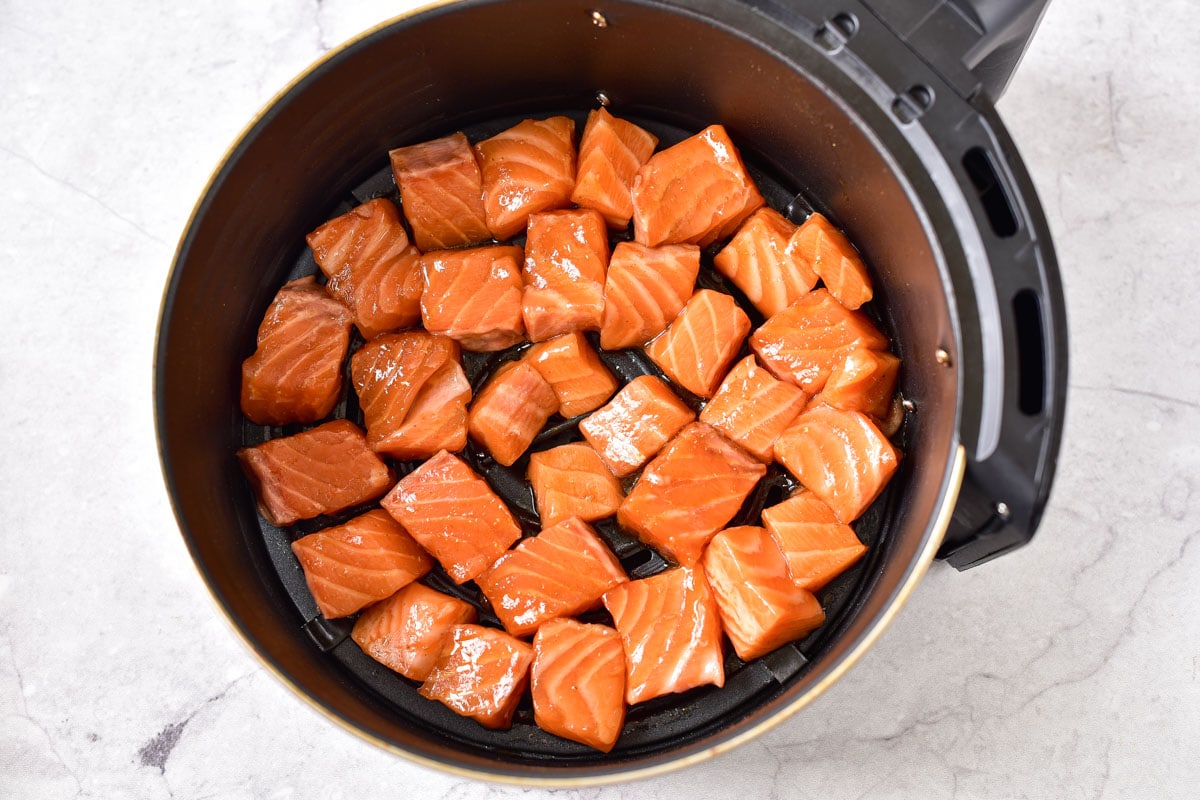 raw salmon cubes places in black round air fryer basket in one layer.