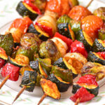 cooked vegetable skewers on wooden sticks sitting on white plate.
