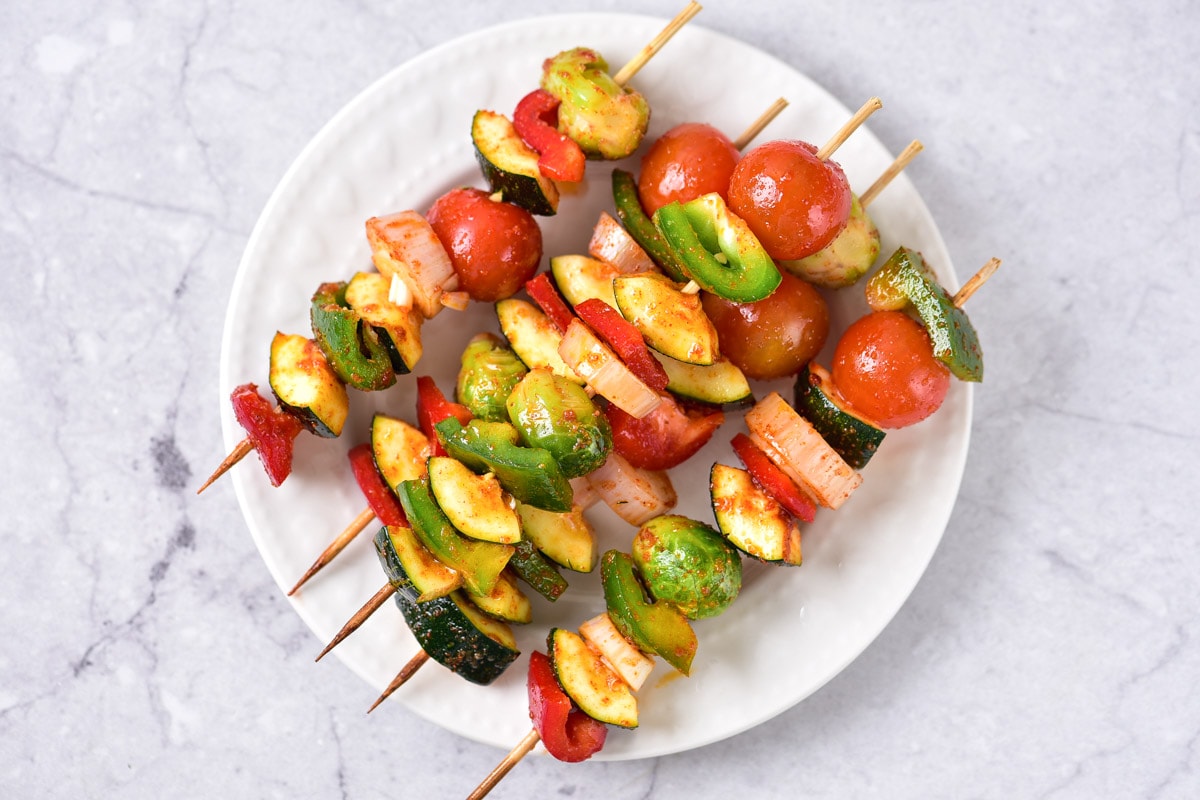 raw vegetable skewers on white plate arranged in a row.