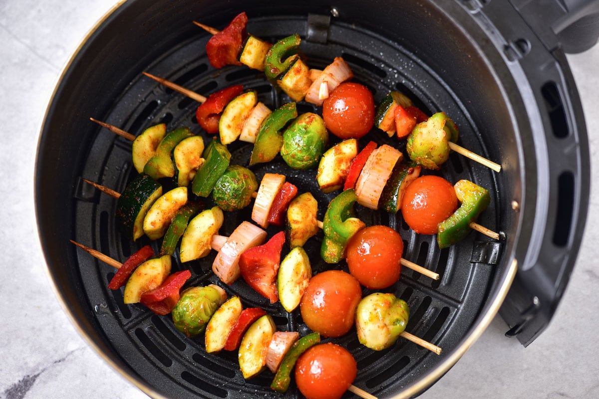 black round air fryer basket filled with vegetable kabobs in a row.