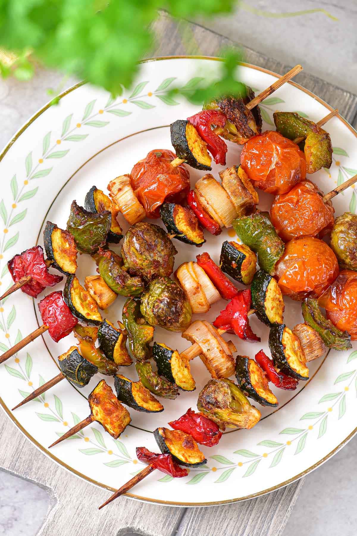 cooked vegetable kabobs on wooden skewers arranged in a row on a white plate.