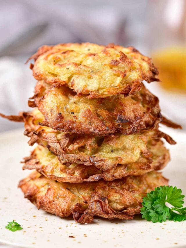 stack of crispy potato pancakes with green herbs beside on white plate.